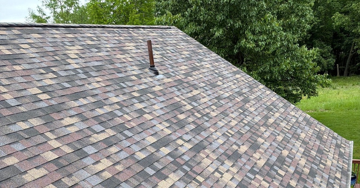 A close-up of the shingled roof of a home with a deck. The shingles are in various colors, including grey, blue, and red.