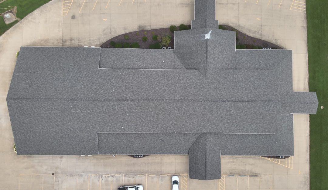 An overhead view of a large commercial building with a multi-layer, multi-slope granule roof and a parking lot.