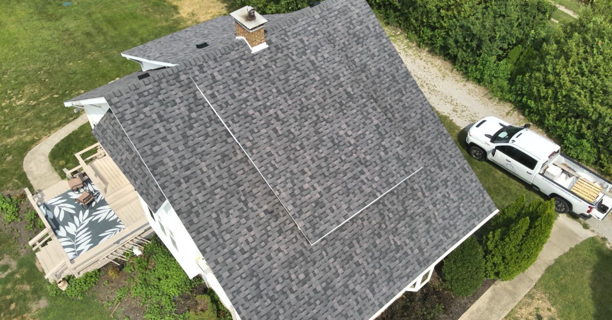An aerial photograph of the roof of a multi-story house with a chimney, granule roof shingles, and a backyard deck.
